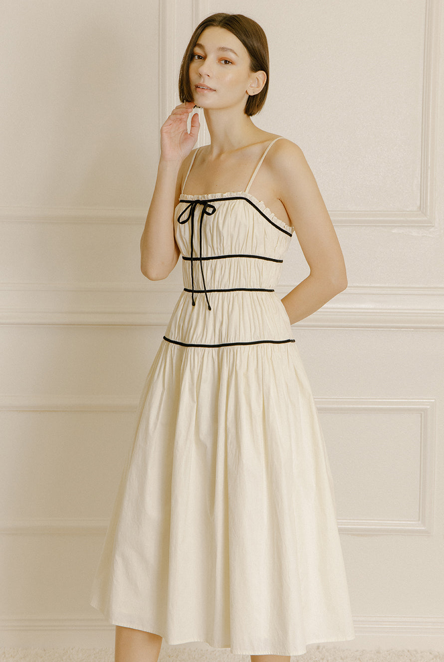 Woman wearing a cream midi dress with black trim against a neutral wall.