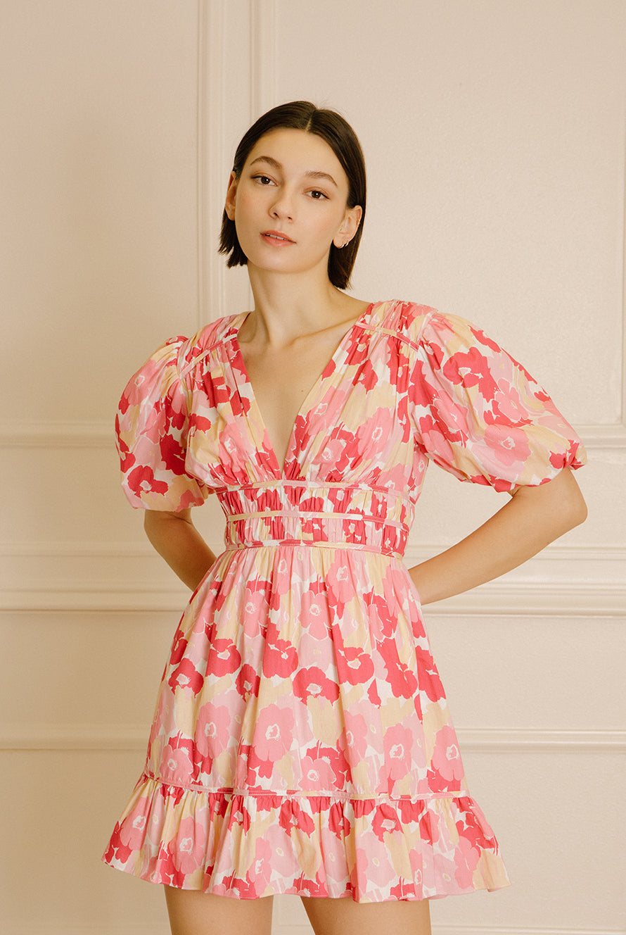 Woman wearing a pink and beige dress with a big floral pattern against a beige wall