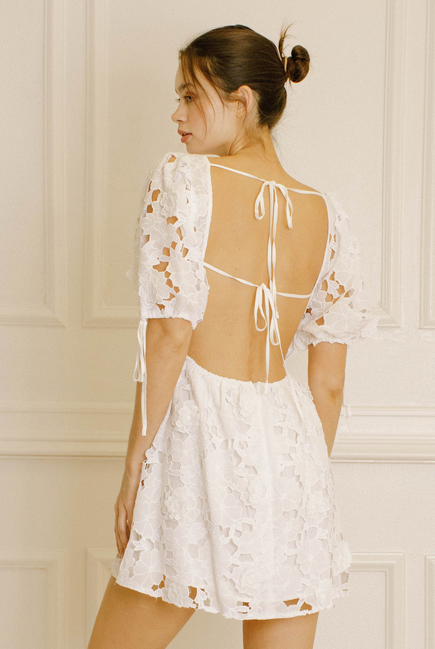 Back view of a woman wearing a white lace dress against a neutral wall