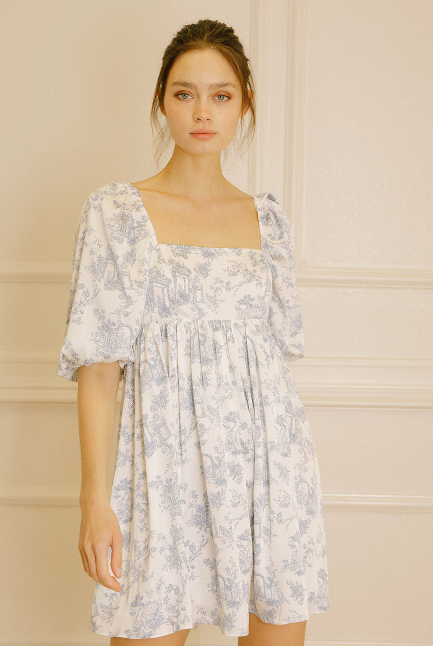 Woman wearing a white dress with a blue garden print against a neutral background