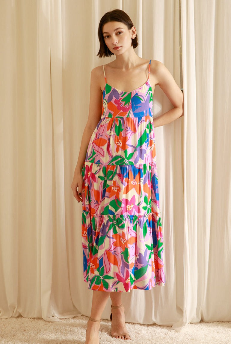 Woman wearing a colorful floral dress standing against a beige curtain.