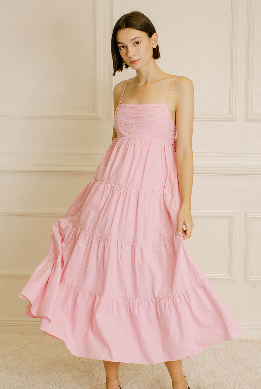 Woman wearing a pink midi dress against a neutral wall.