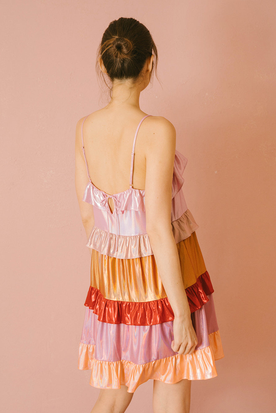 Back view of a woman wearing a colorful iridescent tiered dress against a pink background