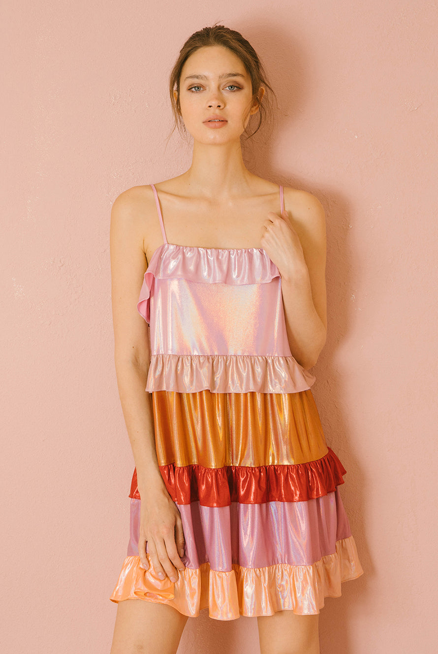 Woman wearing a colorful iridescent tiered dress against a pink background