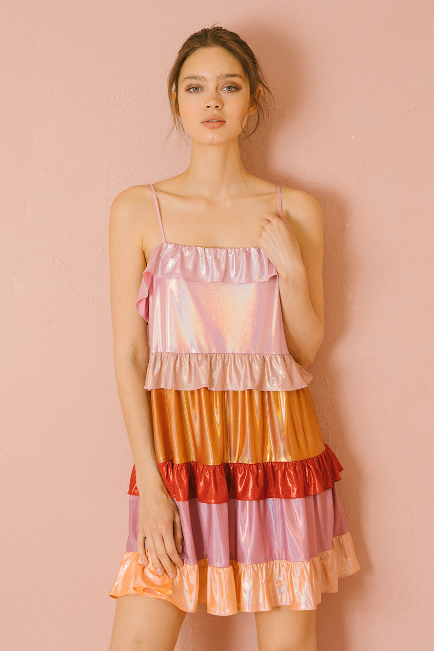 Woman wearing a colorful iridescent tiered dress against a pink background