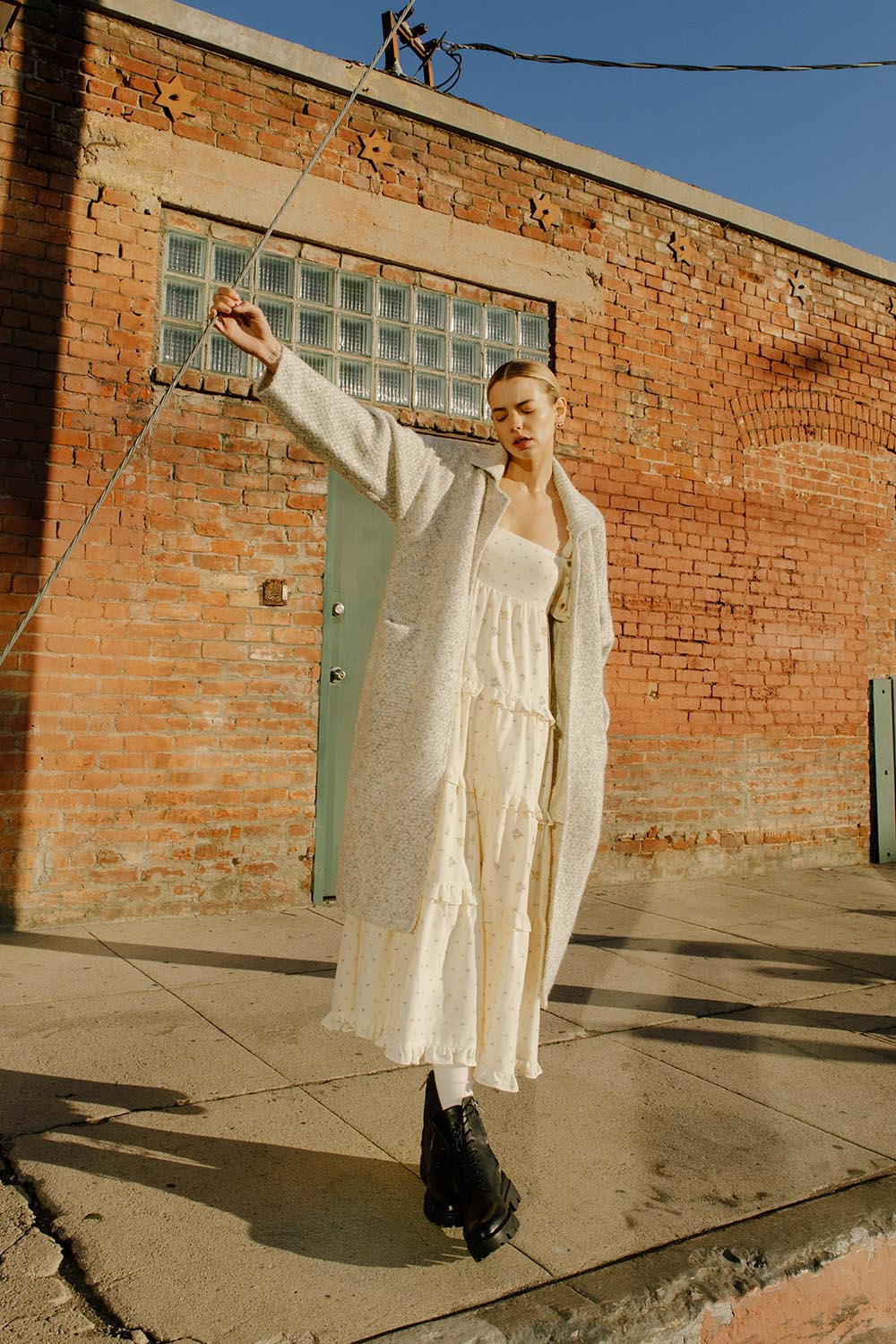 Woman in a long grey cardigan standing against a brick wall.