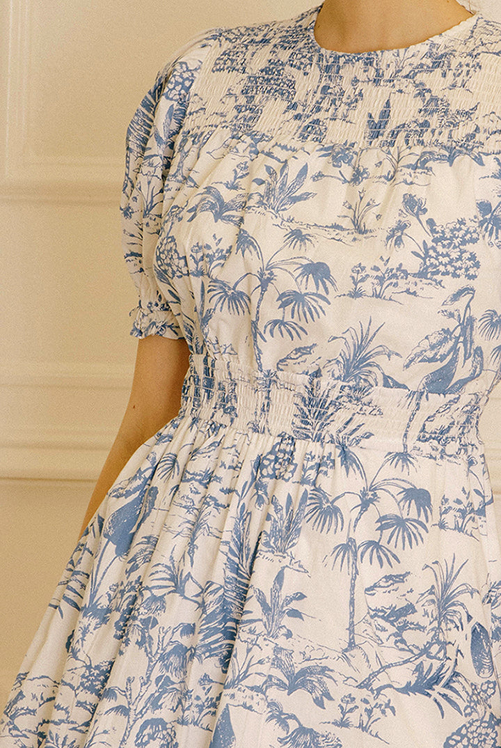 A blue and white tropical print dress against a beige wall.