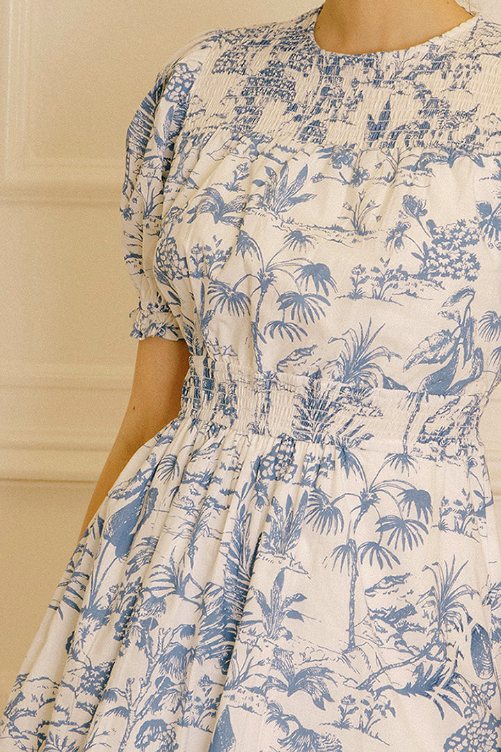 A blue and white tropical print dress against a beige wall.