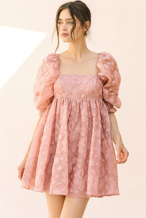 Woman wearing a pink dress with puff sleeves against a beige background