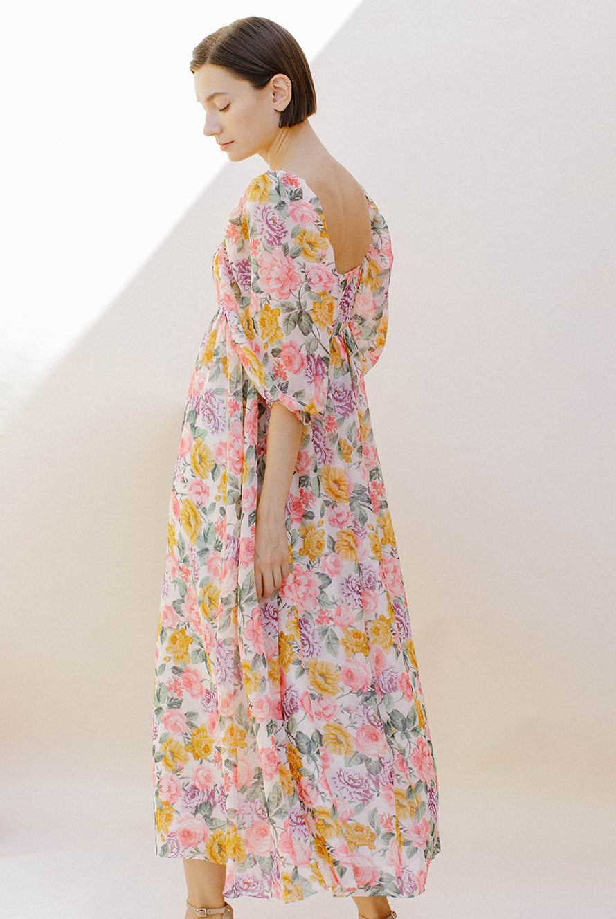 Side view of a woman wearing a pink floral midi dress against a plain background