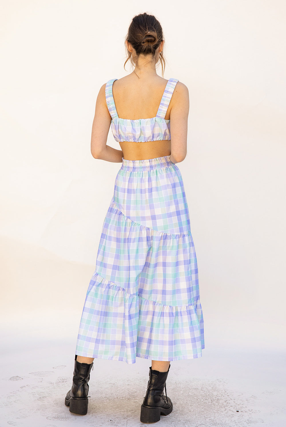 Back view of a woman wearing a pastel plaid top and skirt set with a white background
