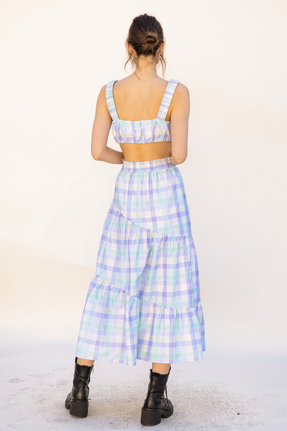 Back view of a woman wearing a pastel plaid top and skirt set with a white background