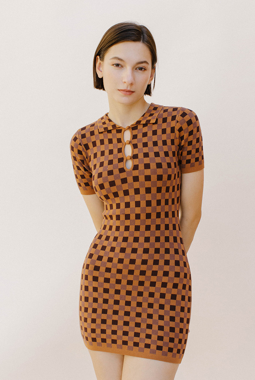 Woman wearing a brown and dark brown checkered dress against a plain background
