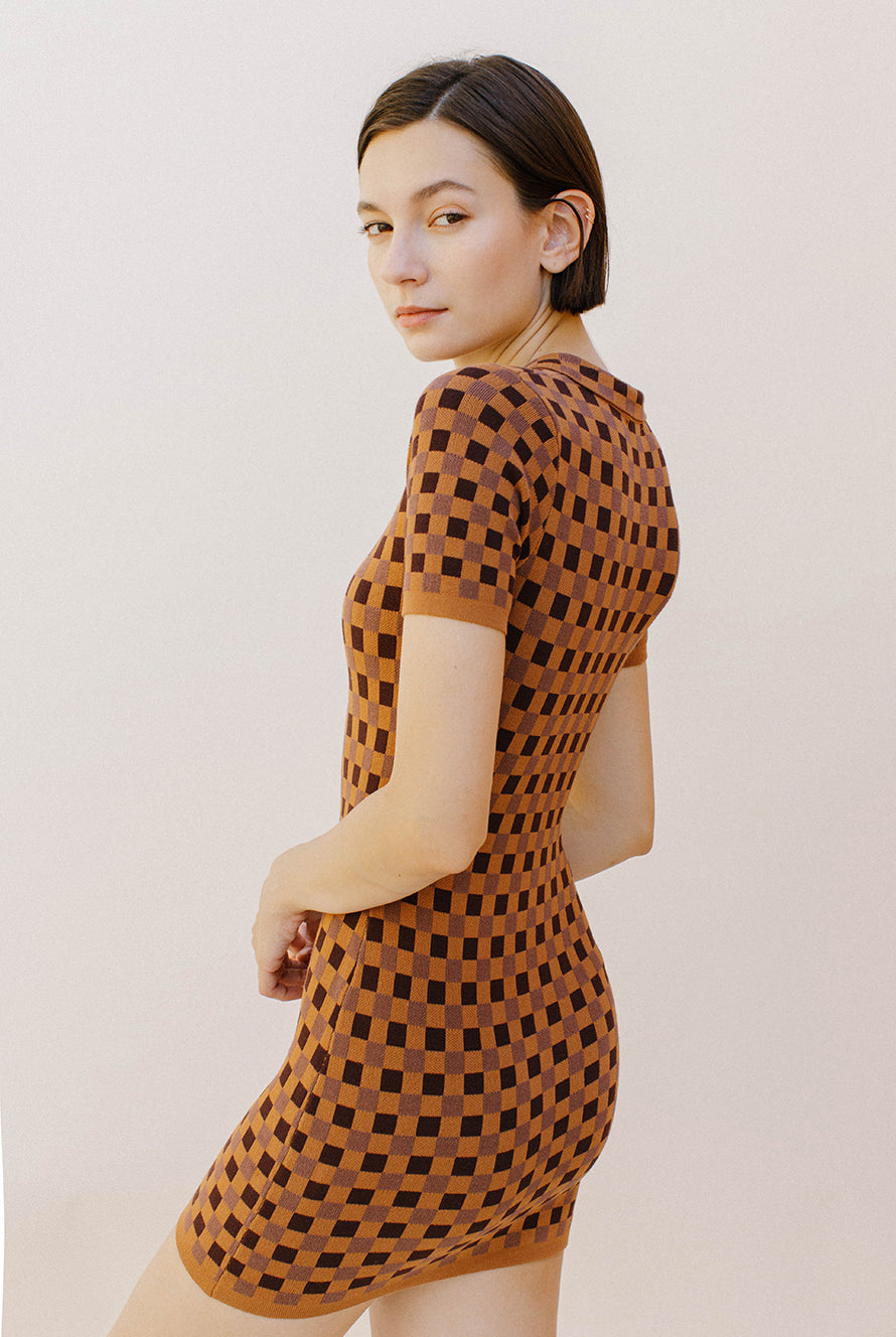 Side view of a woman wearing a brown and dark brown checkered dress against a plain background