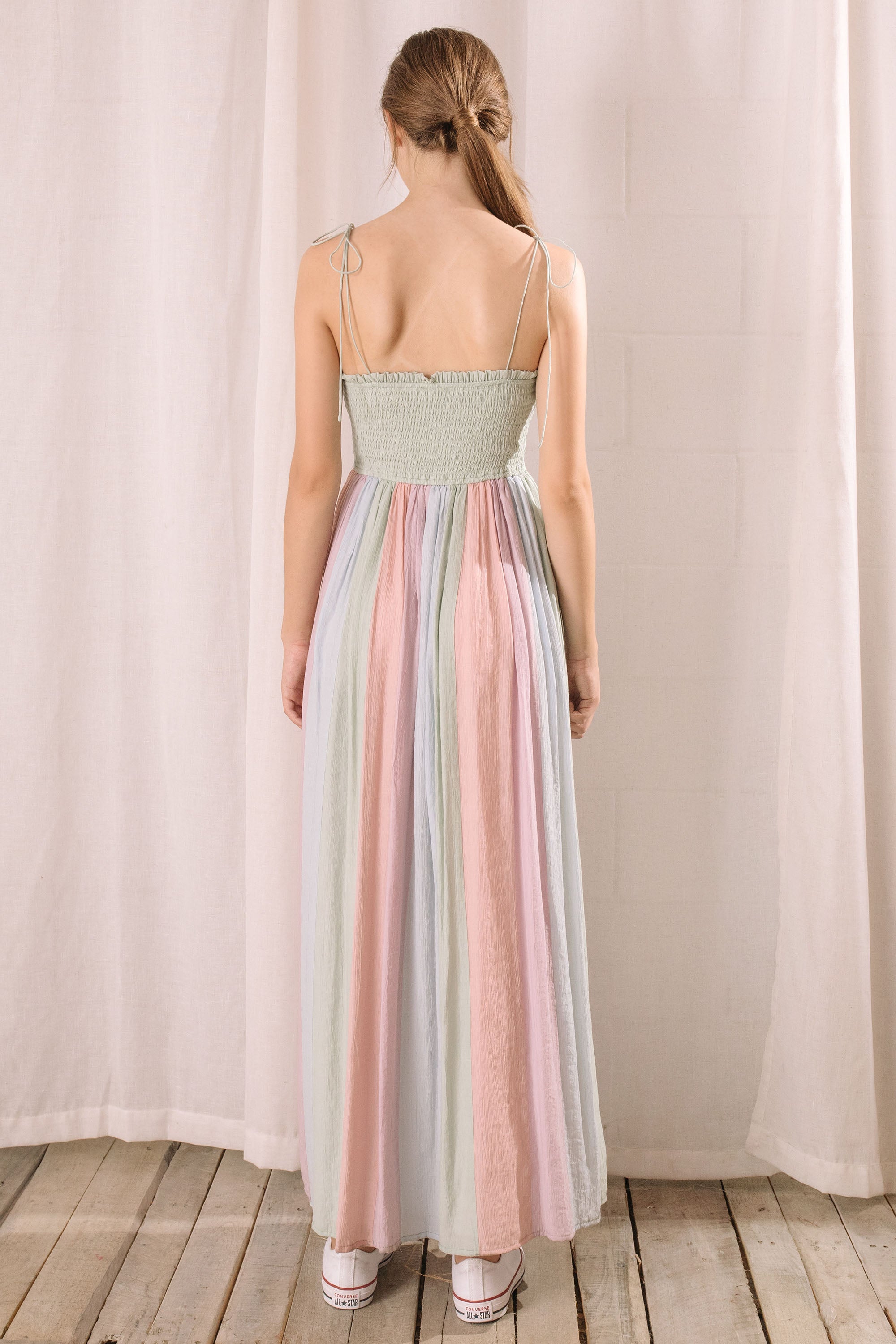 Back view of a woman wearing a pastel striped dress standing against a plain background