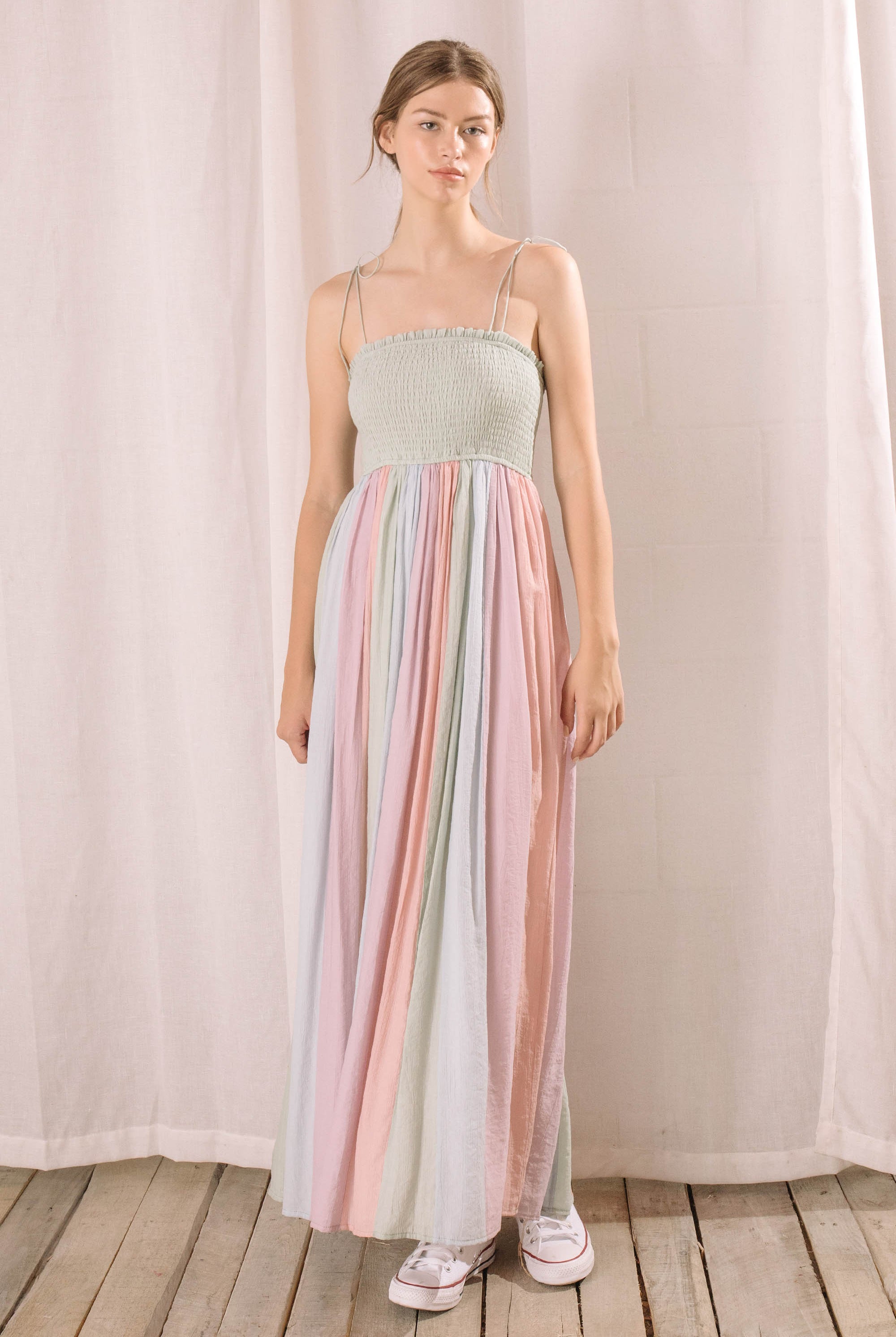 Woman wearing a pastel striped dress standing against a plain background