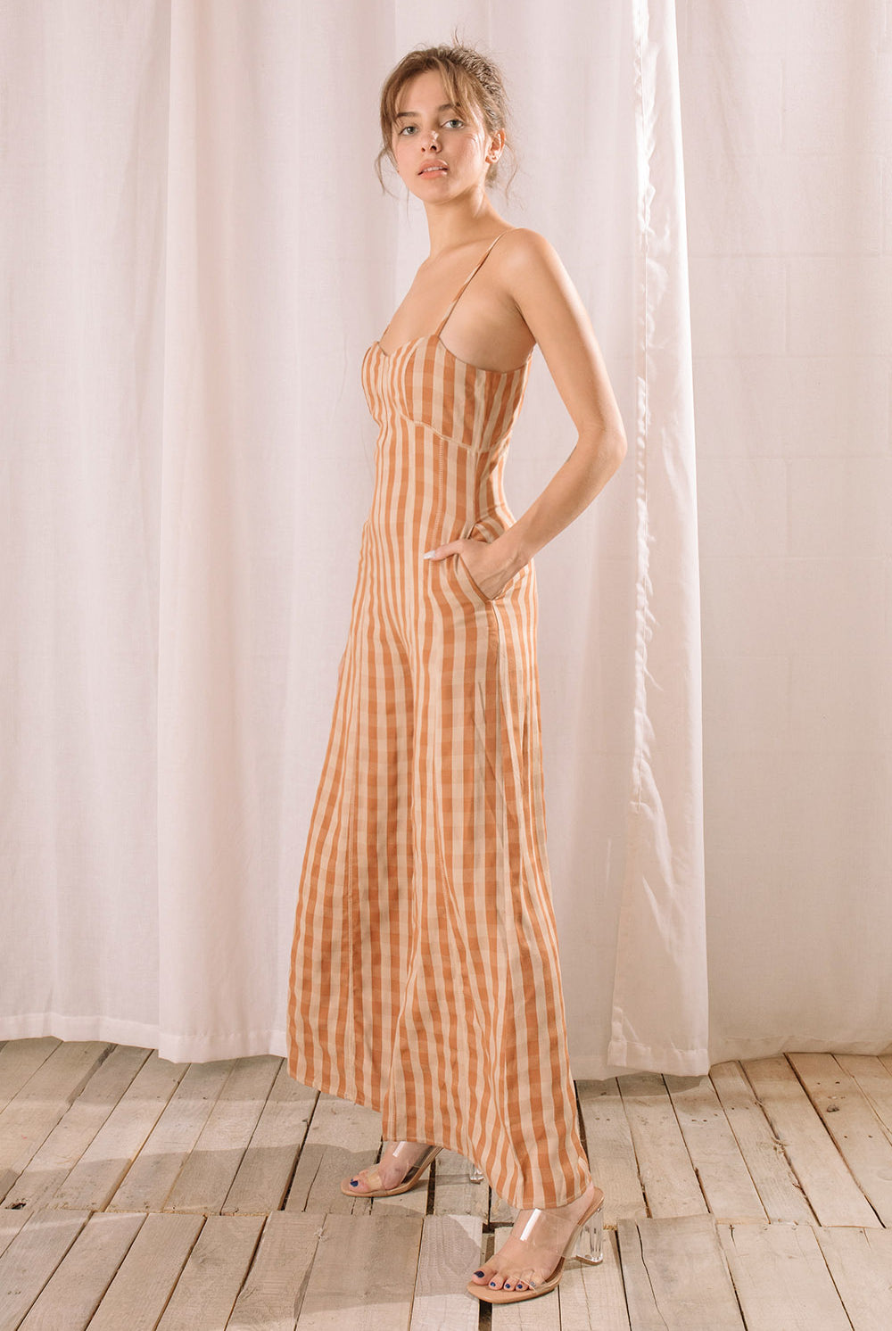 Side view of a person wearing an orange checkered jumpsuit standing against a white curtain.