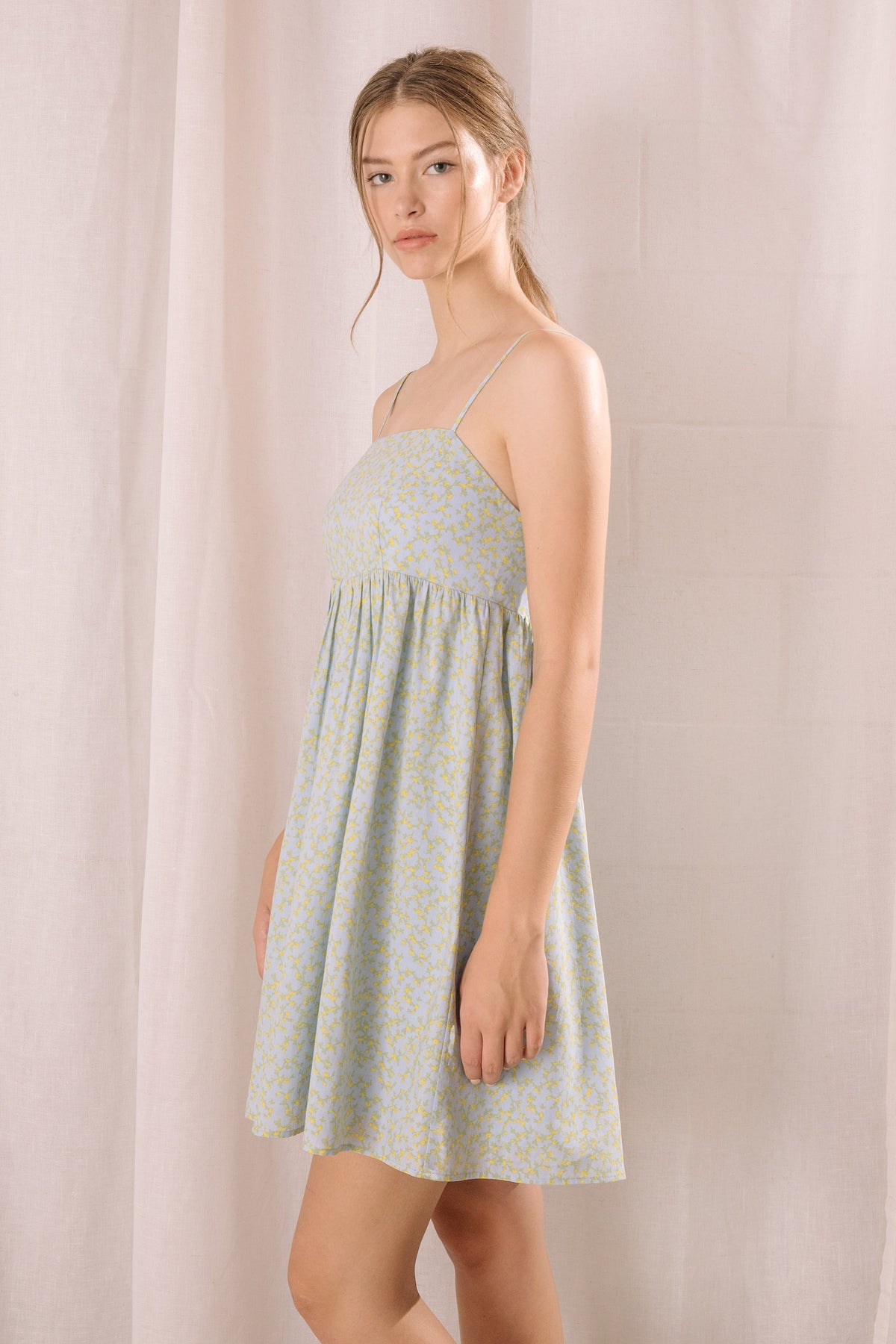 Side view of a woman wearing a light blue dress against a plain background