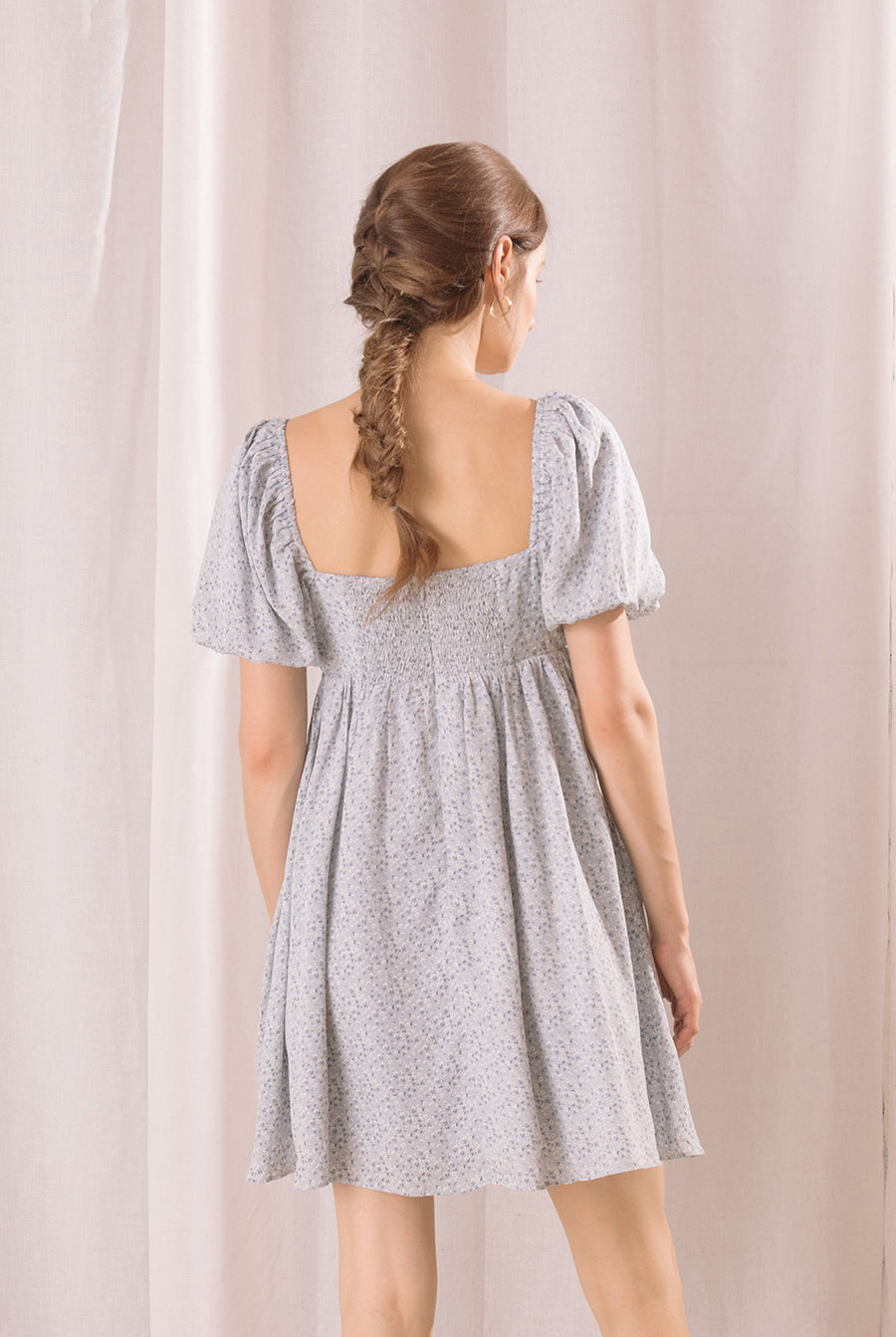 Back view of a woman wearing a light blue floral dress against a plain background