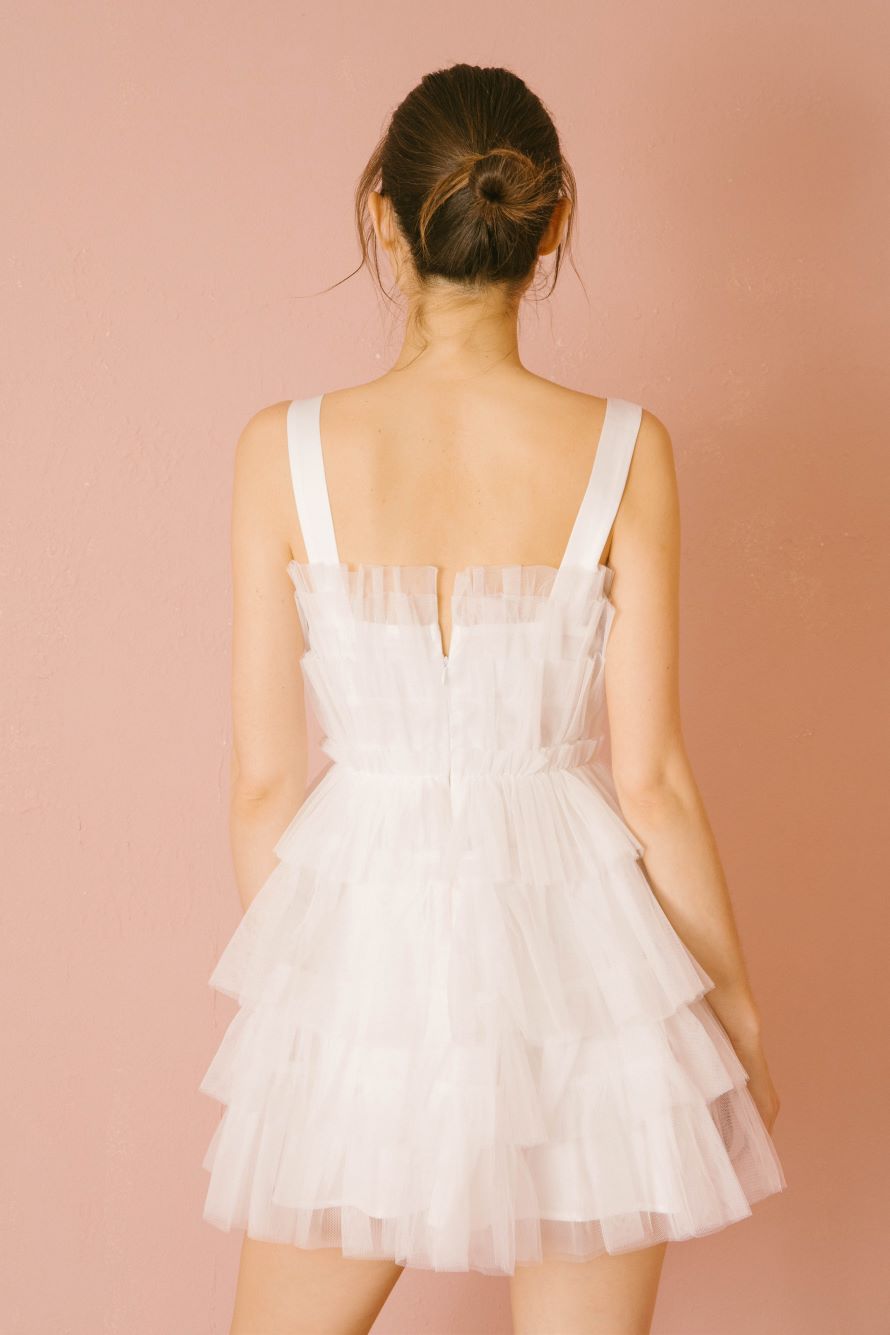 Back of a woman wearing a white tiered dress against a pink background