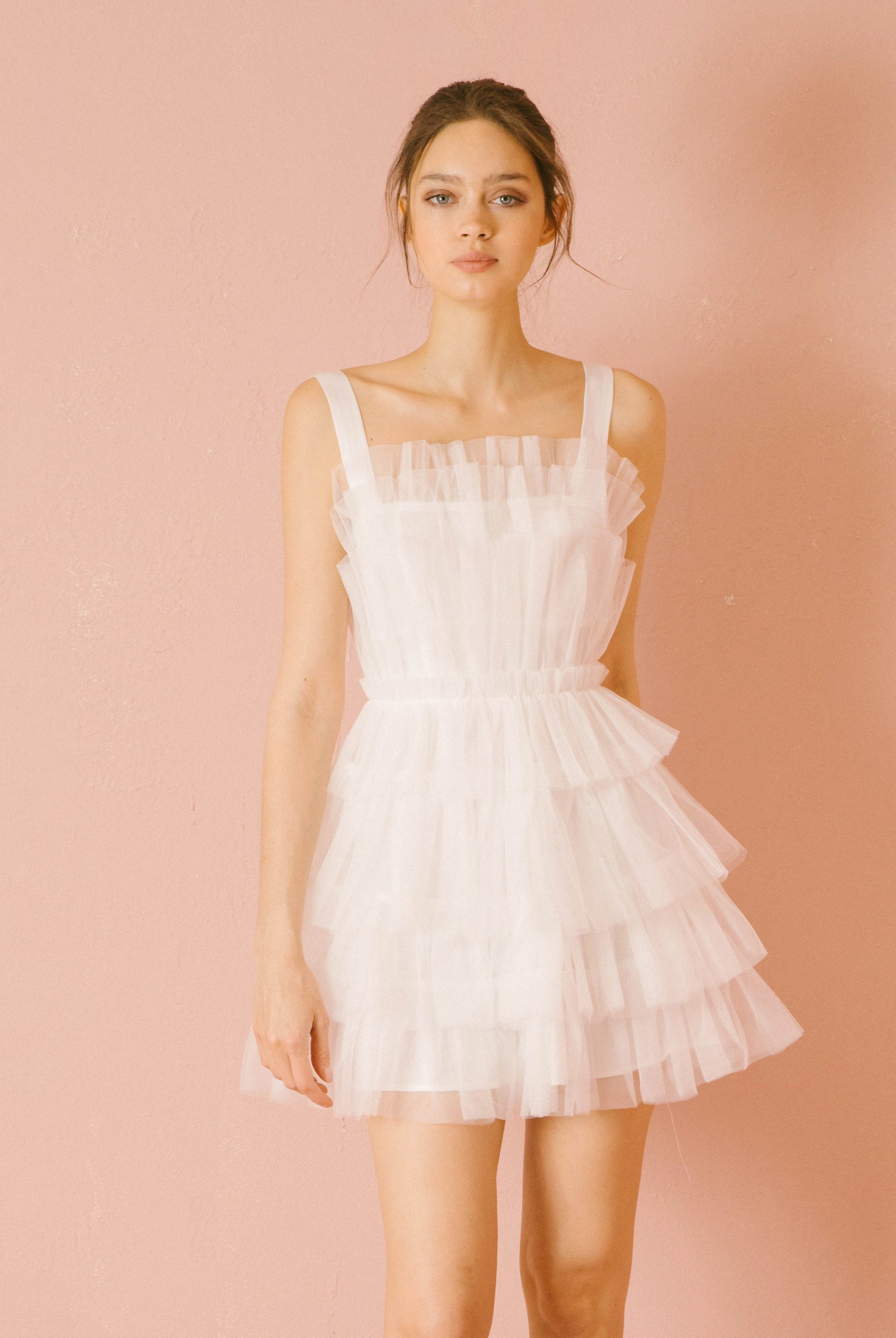 Woman wearing a white tiered dress against a pink background