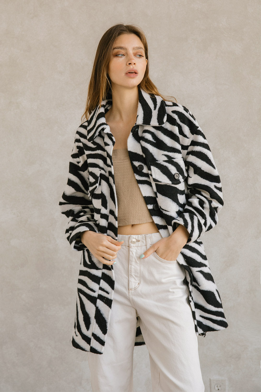 Woman wearing a zebra-patterned coat and white jeans against a plain background