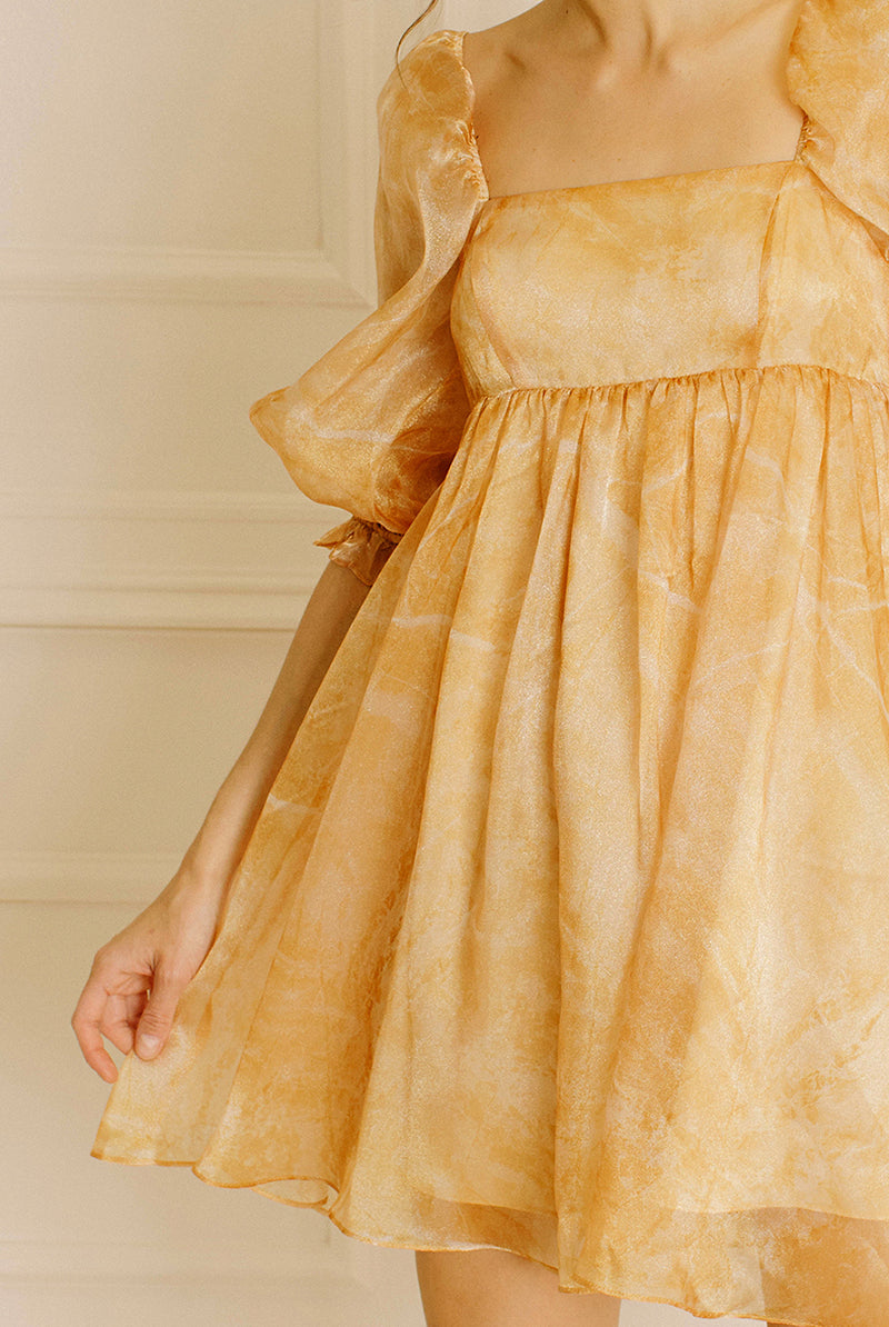 A yellow dress with puff sleeves against a neutral wall.