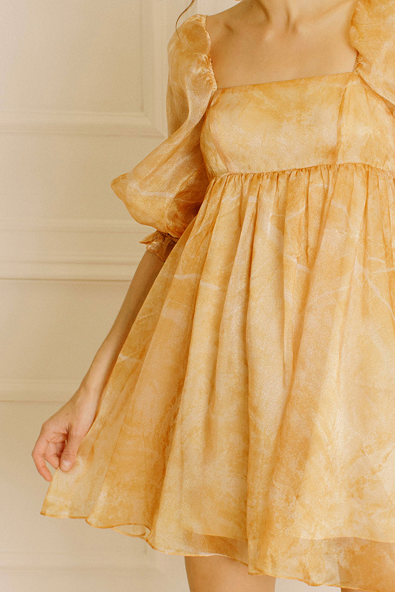 A yellow dress with puff sleeves against a neutral wall.