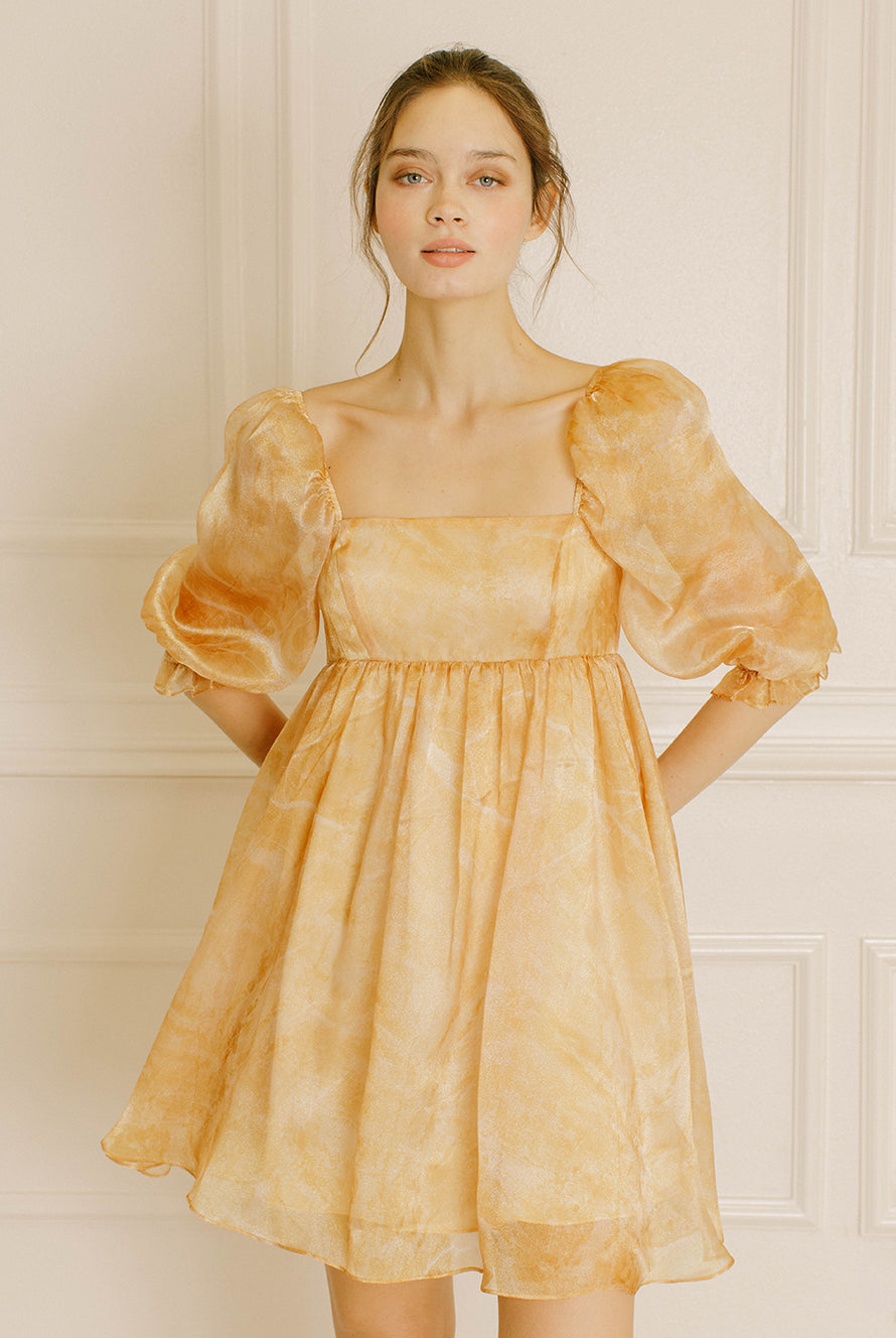 Woman wearing a yellow dress with puff sleeves against a neutral wall.