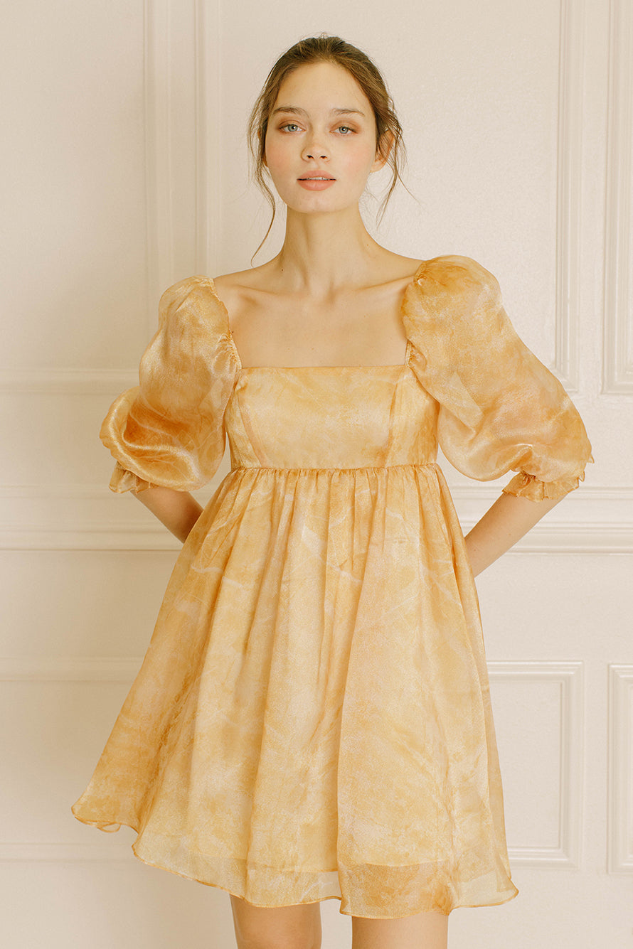 Woman wearing a yellow dress with puff sleeves against a neutral wall.