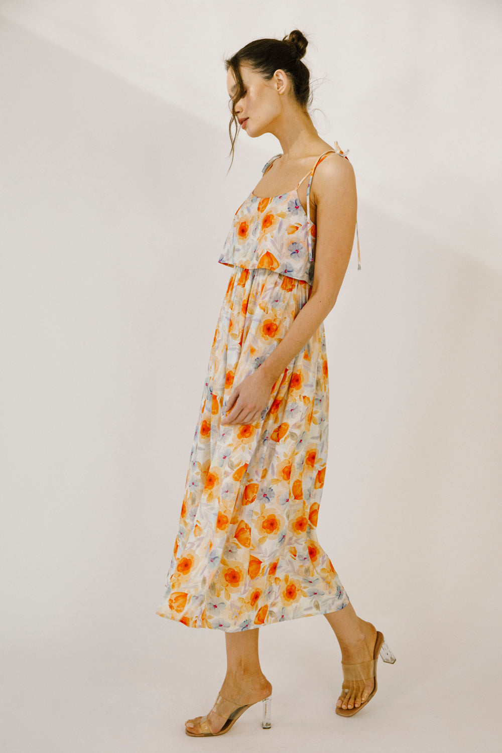 A woman modeling a colorful floral print midi dress against a neutral wall.