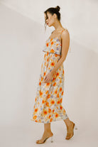 A woman modeling a colorful floral print midi dress against a neutral wall.