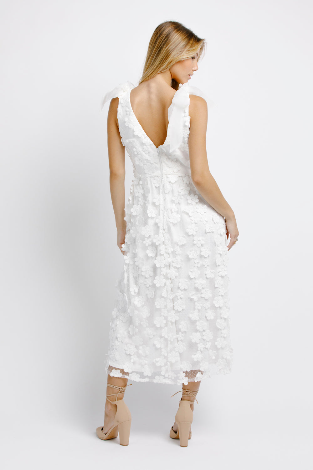 Back view of a woman wearing a white floral dress on a white background