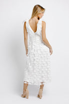 Back view of a woman wearing a white floral dress on a white background