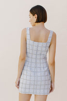 Back view of a woman wearing a light blue tweed  dress against a plain background