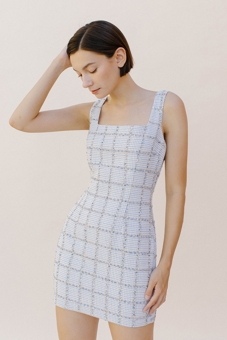  Side view of a woman wearing a light blue tweed  dress against a plain background