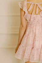 Pink dress with a cherry blossom print, self-tie bow and smocked upper back against a neutral background