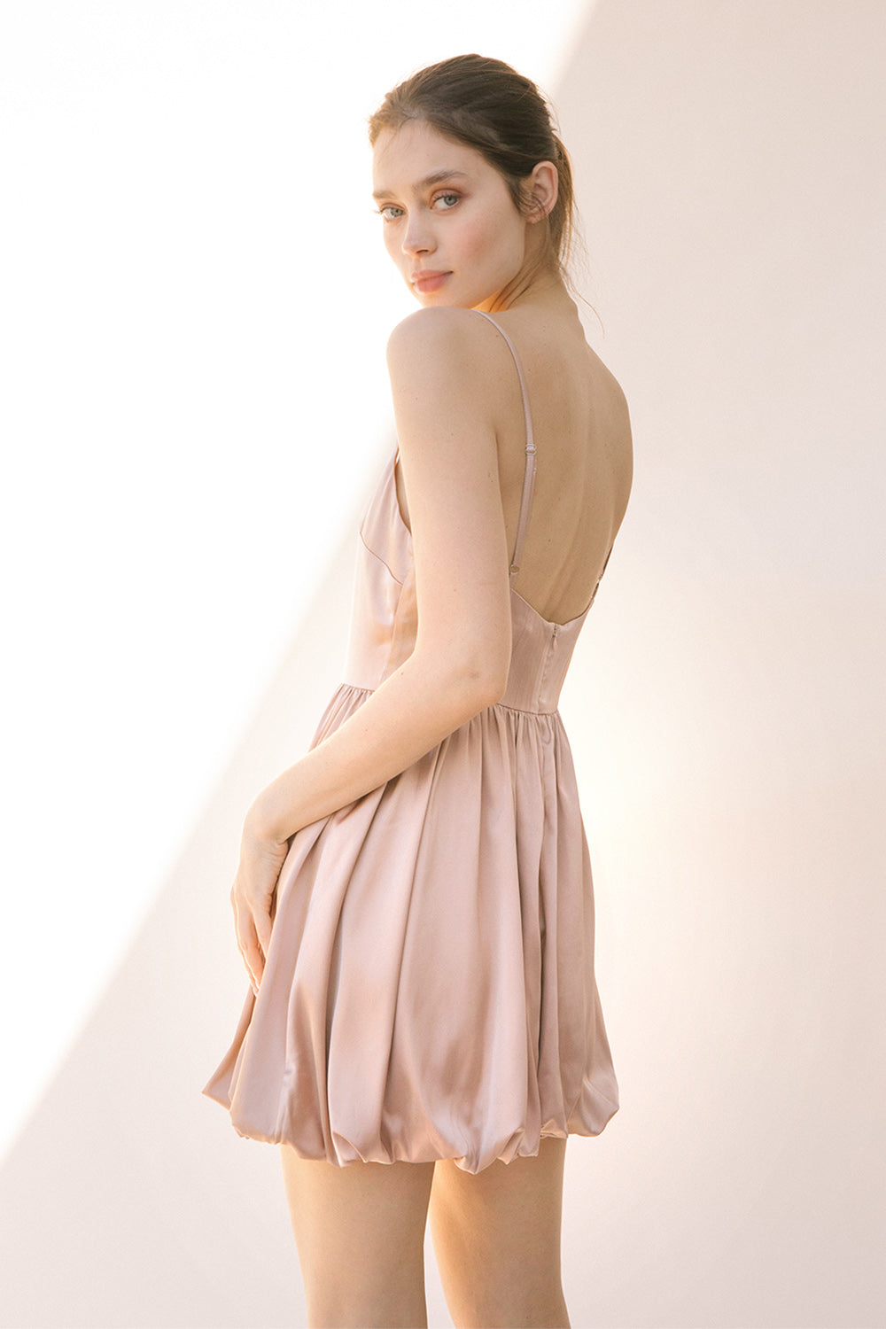 Back view of a woman wearing a sheer beige dress against a plain background
