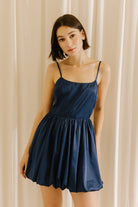 Woman wearing a navy blue dress against a beige curtain background
