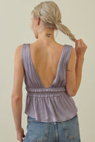 A woman shown from the back wearing a sleeveless lavender top with an open back and gathered waist, paired with blue jeans against a plain light beige background.