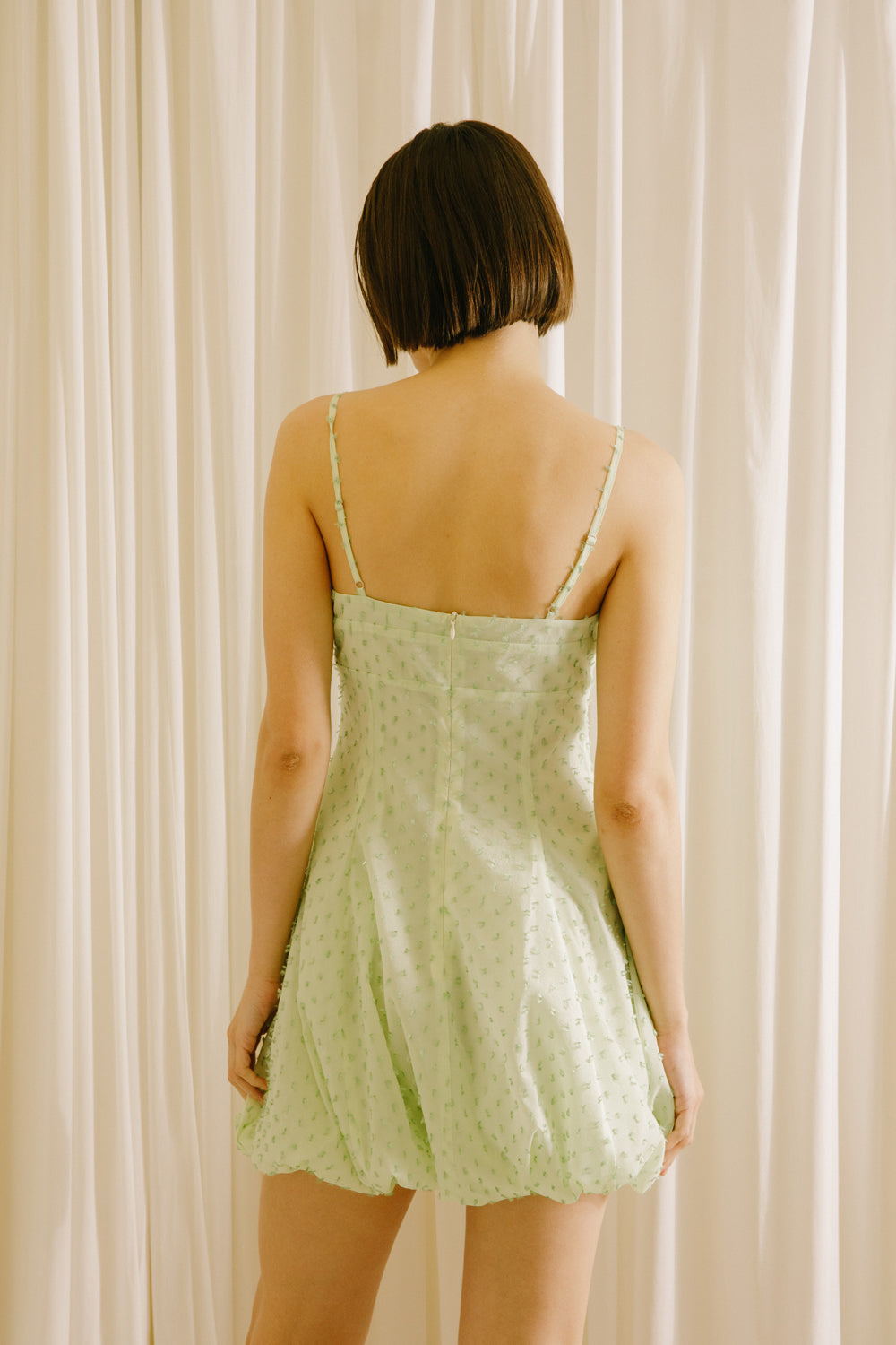 Back view of a woman wearing a mint polka dot mini dress against a white background