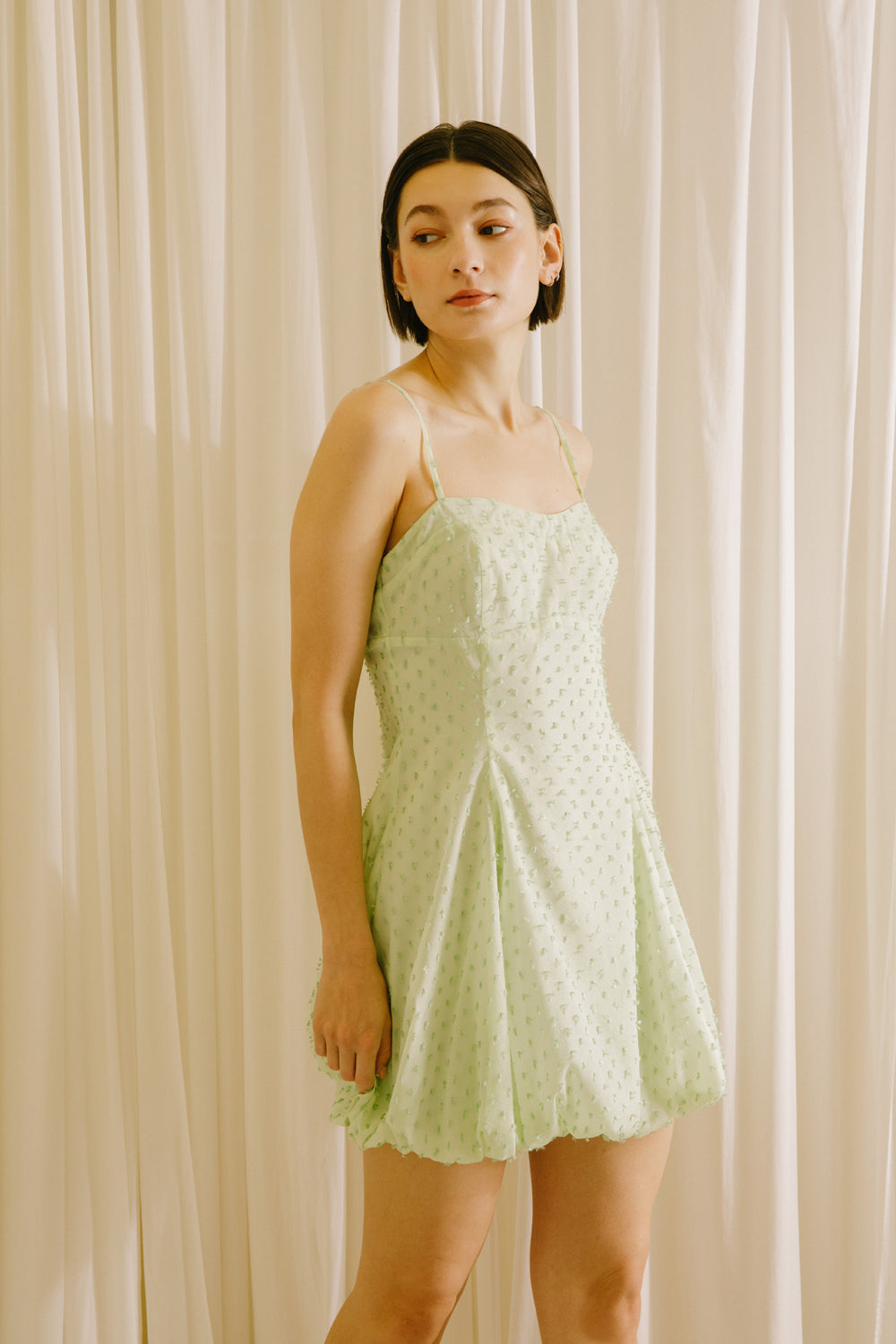 Side view of a woman wearing a mint polka dot mini dress against a white background
