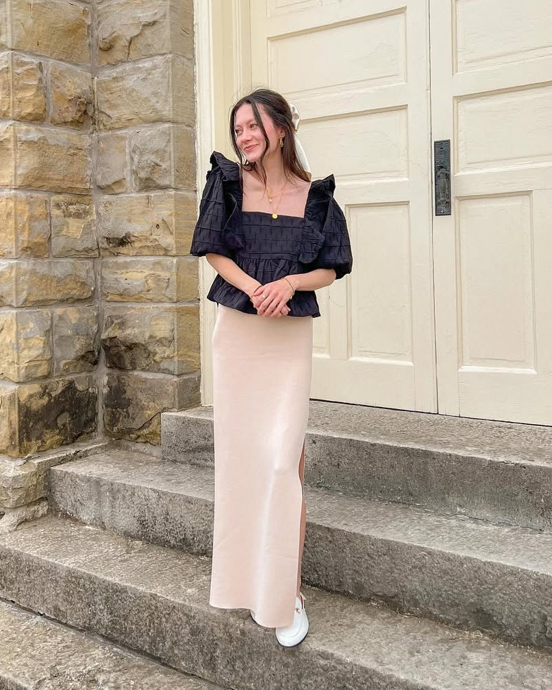 Woman wearing a black blouse standing on steps in front of a large door.