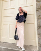 Woman wearing a black blouse and cream skirt posing in front of a large door with stone walls.
