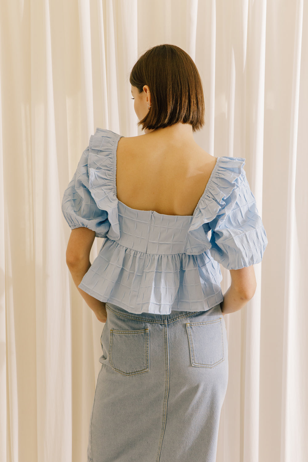 A back view of a model wearing a blue top with a back invisible zipper and a light denim midi skirt