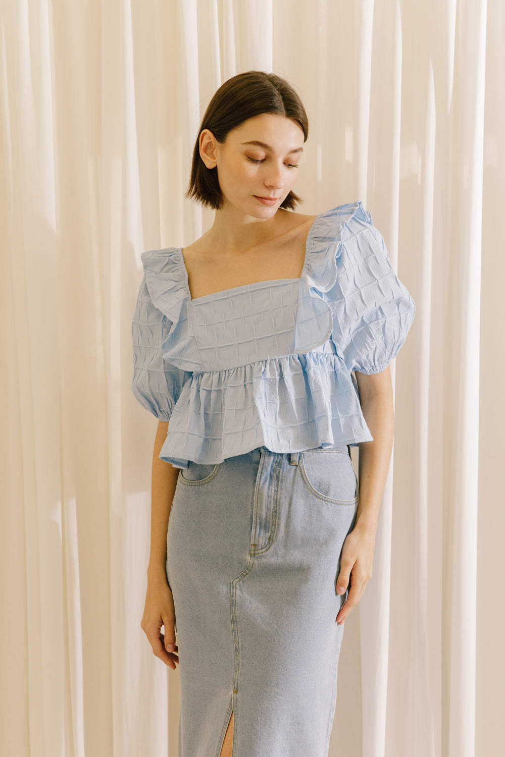 A model wearing a blue top with a light denim midi skirt