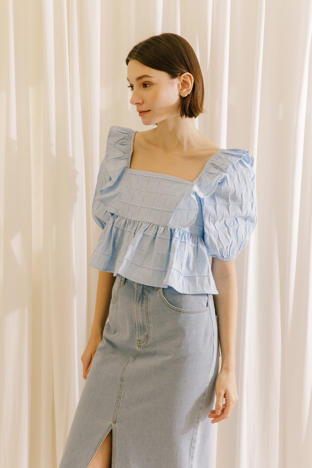 Side view of a model wearing a blue top with a back invisible zipper and a light denim midi skirt