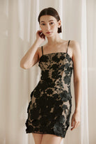 Woman wearing a black floral embroidery dress against a white curtain background