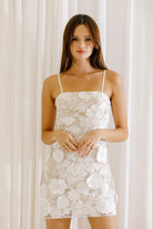 Woman wearing a white 3D floral embroidery mini dress against a white curtain background