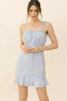 Woman wearing a blue checkered dress with small red daisy print on a beige background